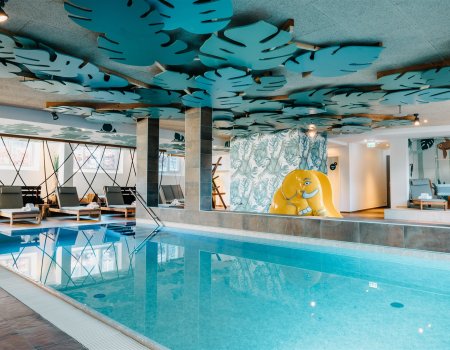 Innenpool mit Liegestühlen, blauen Blattformen an der Decke und gelbem Elefantenrutsch