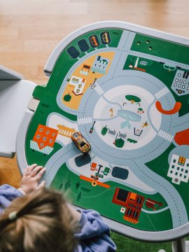 Kind spielt mit einem Spieltisch mit Straßenkarte und einem kleinen Spielzeugauto