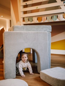 Kleines Kind krabbelt unter einem gepolsterten Spieltunnel im Kinderzimmer